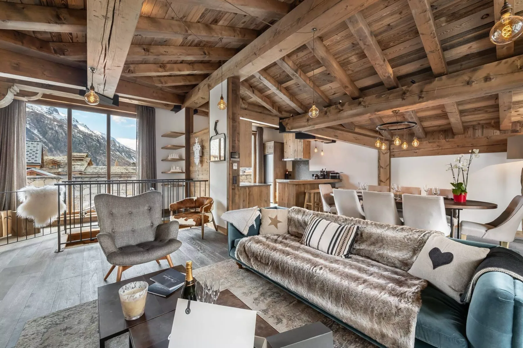A living room with seating beneath exposed wooden ceiling beams and large windows.