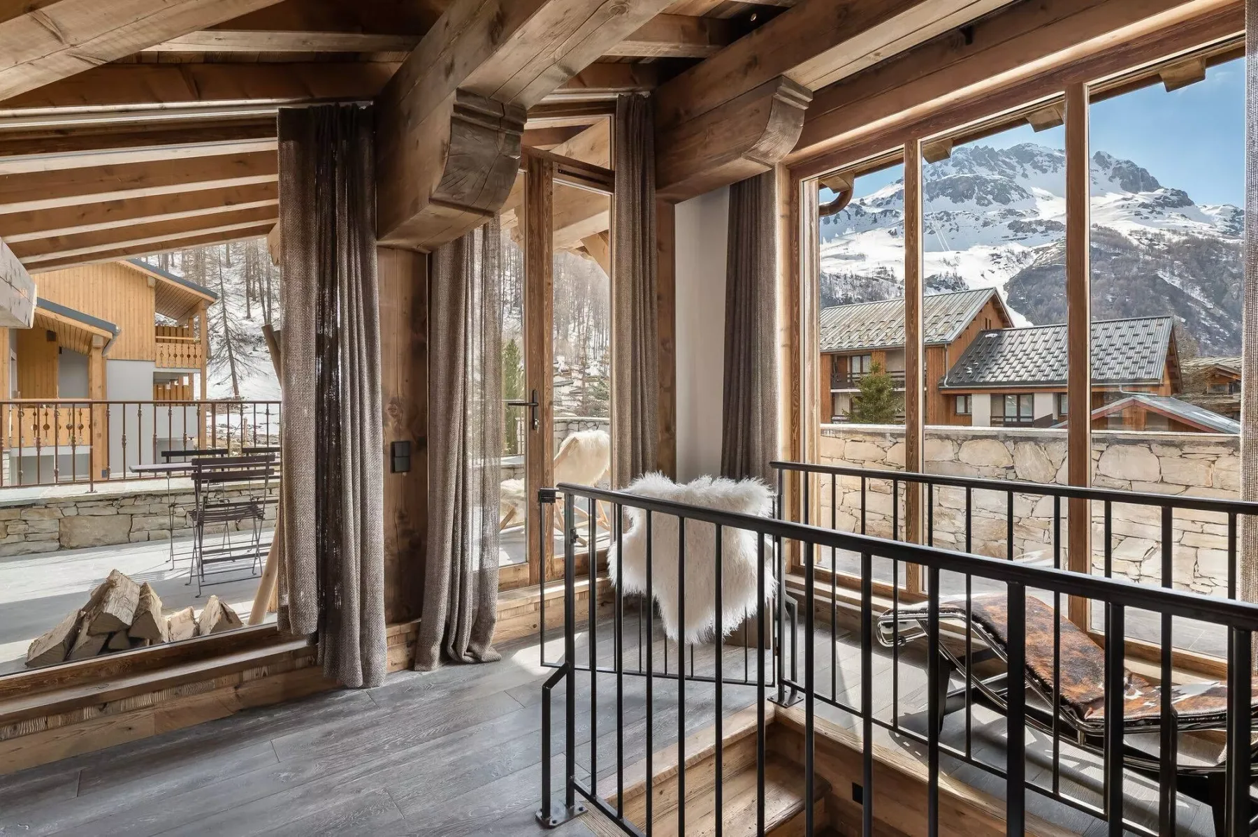 A timber-framed balcony overlooks neighboring buildings and snowy mountains.