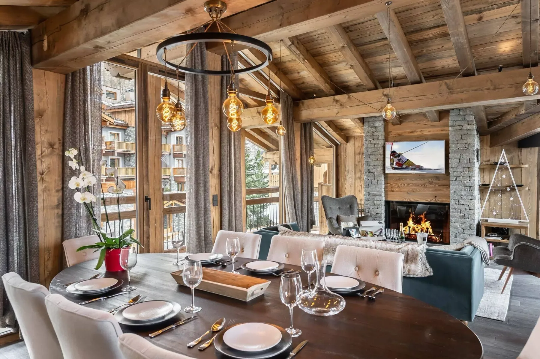 A dining area opens onto a living room with a stone fireplace and exposed timber ceiling.