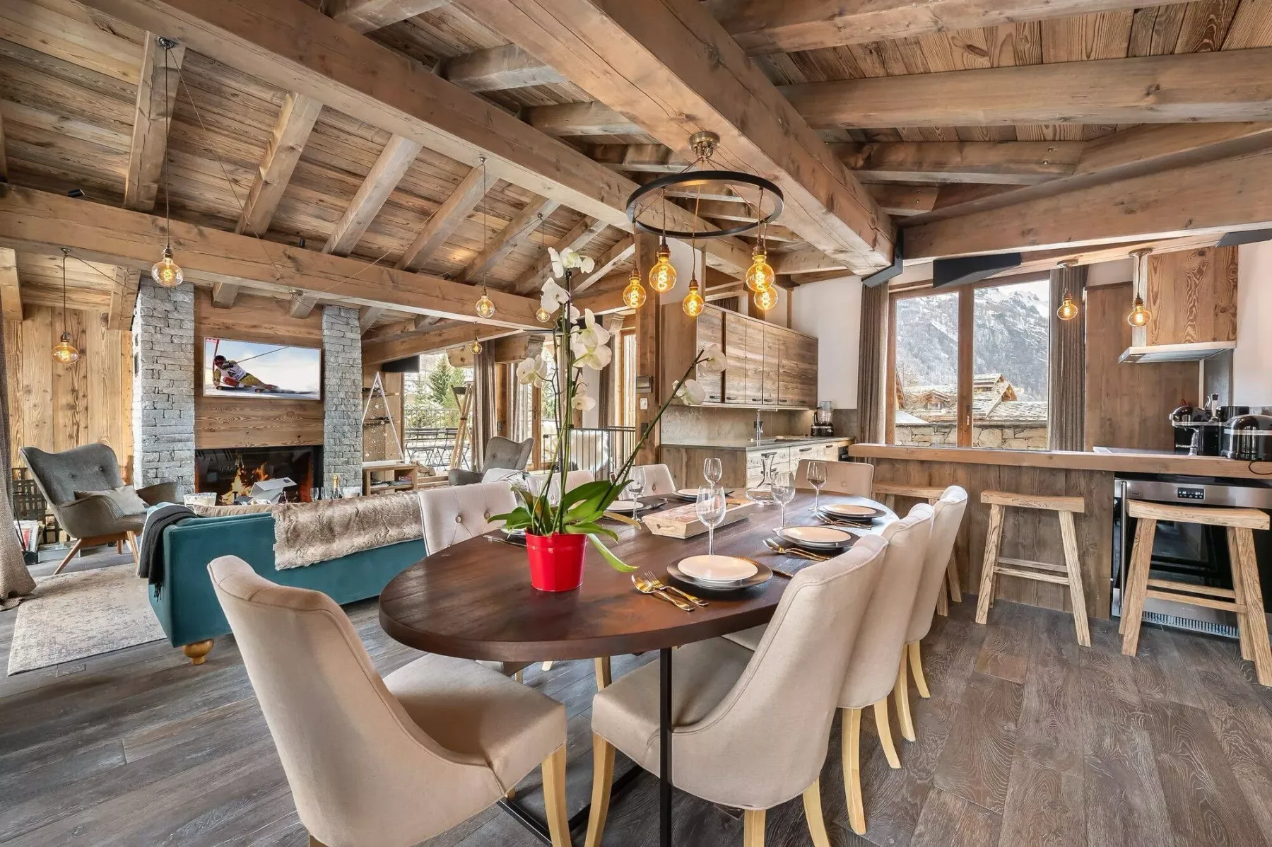 A rustic open-plan living and dining area with a long table beneath exposed wooden beams.