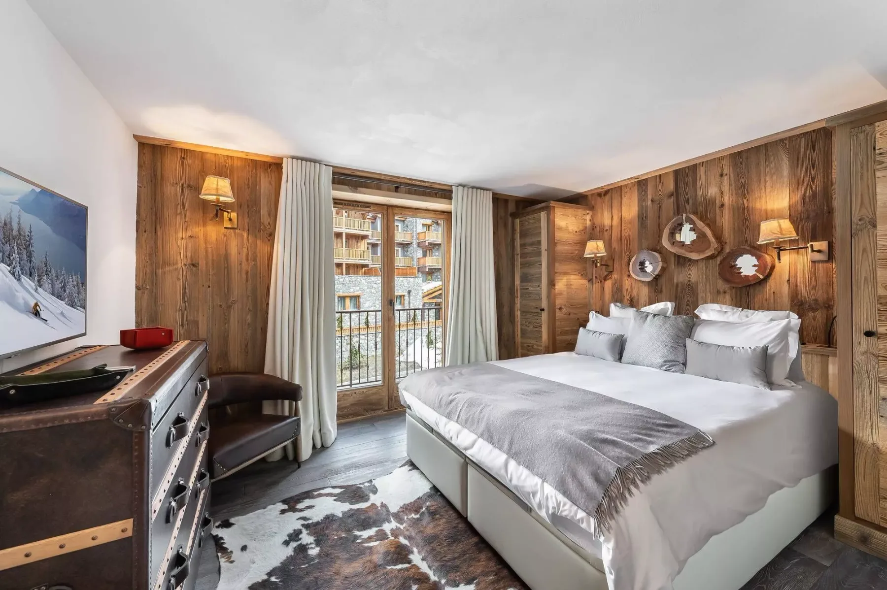 A bedroom with a large bed, wood-paneled walls, and a window with curtains.