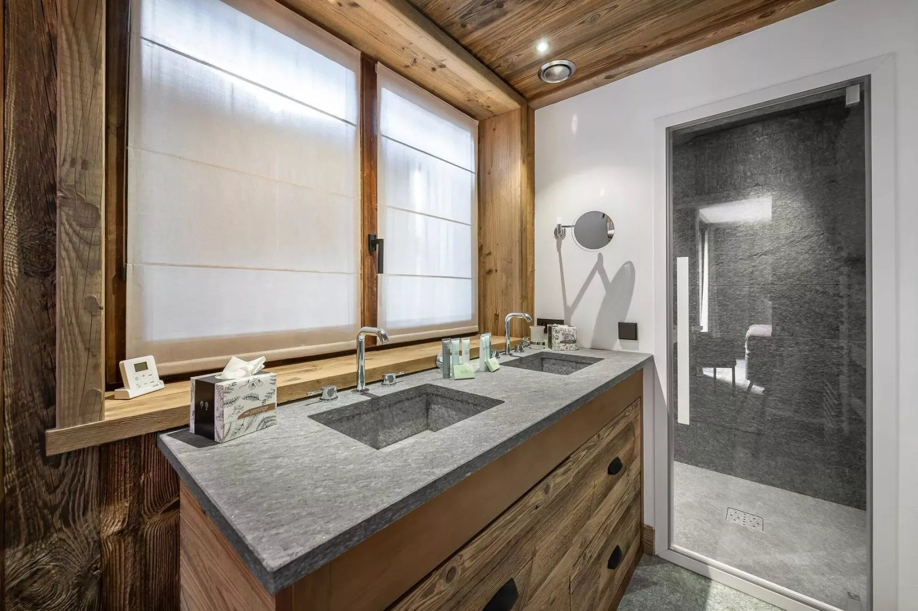 A bathroom vanity with two sinks sits beside a glass-enclosed shower.