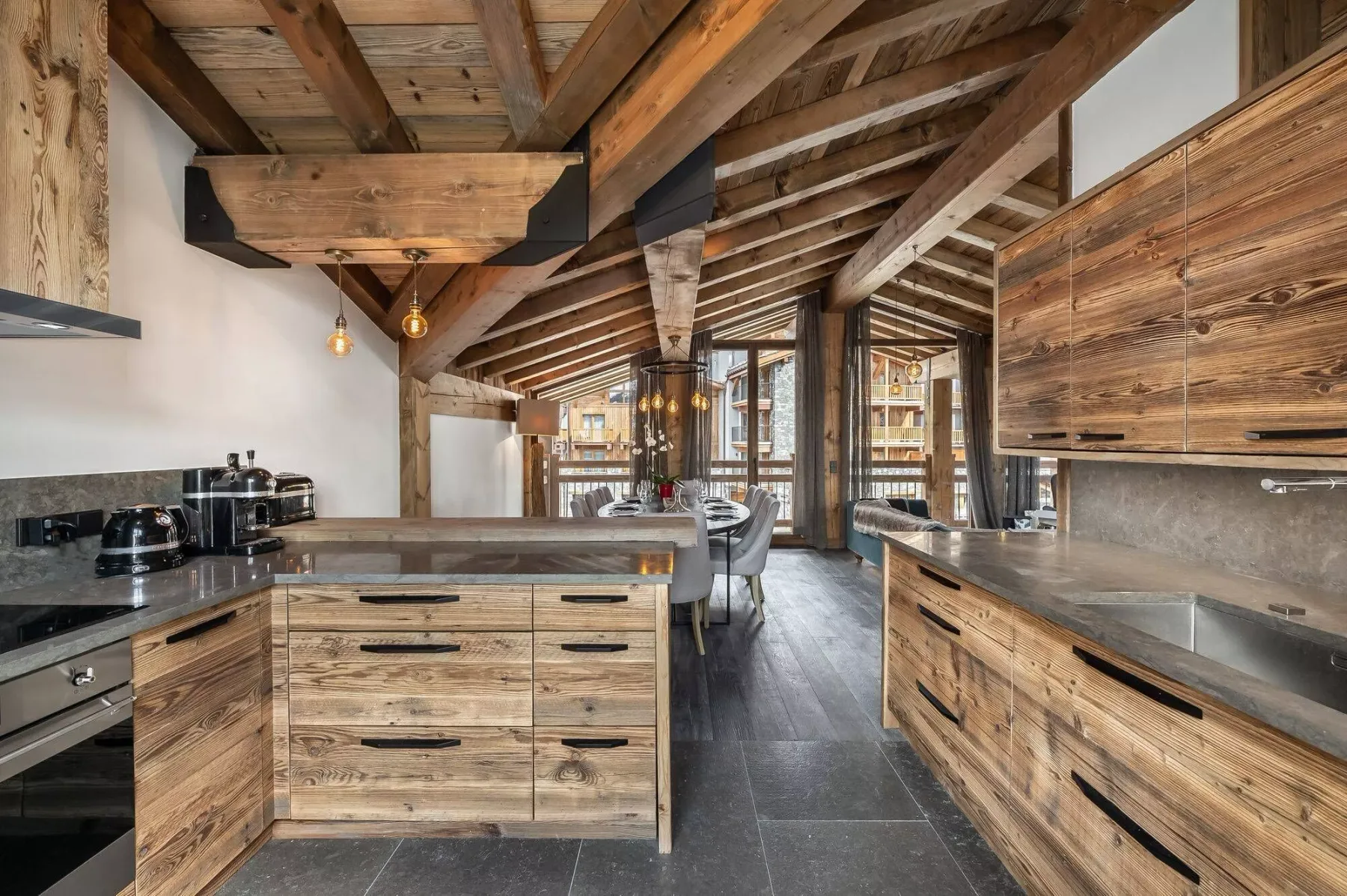 A spacious kitchen with wooden cabinetry, dark countertops, and exposed ceiling beams.