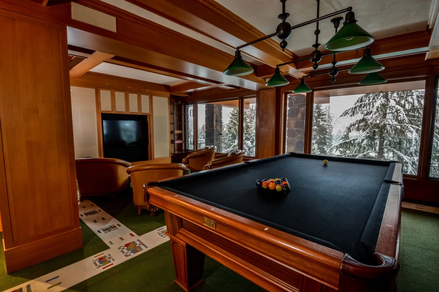 A billiards room with a pool table and large windows overlooking snowy trees.