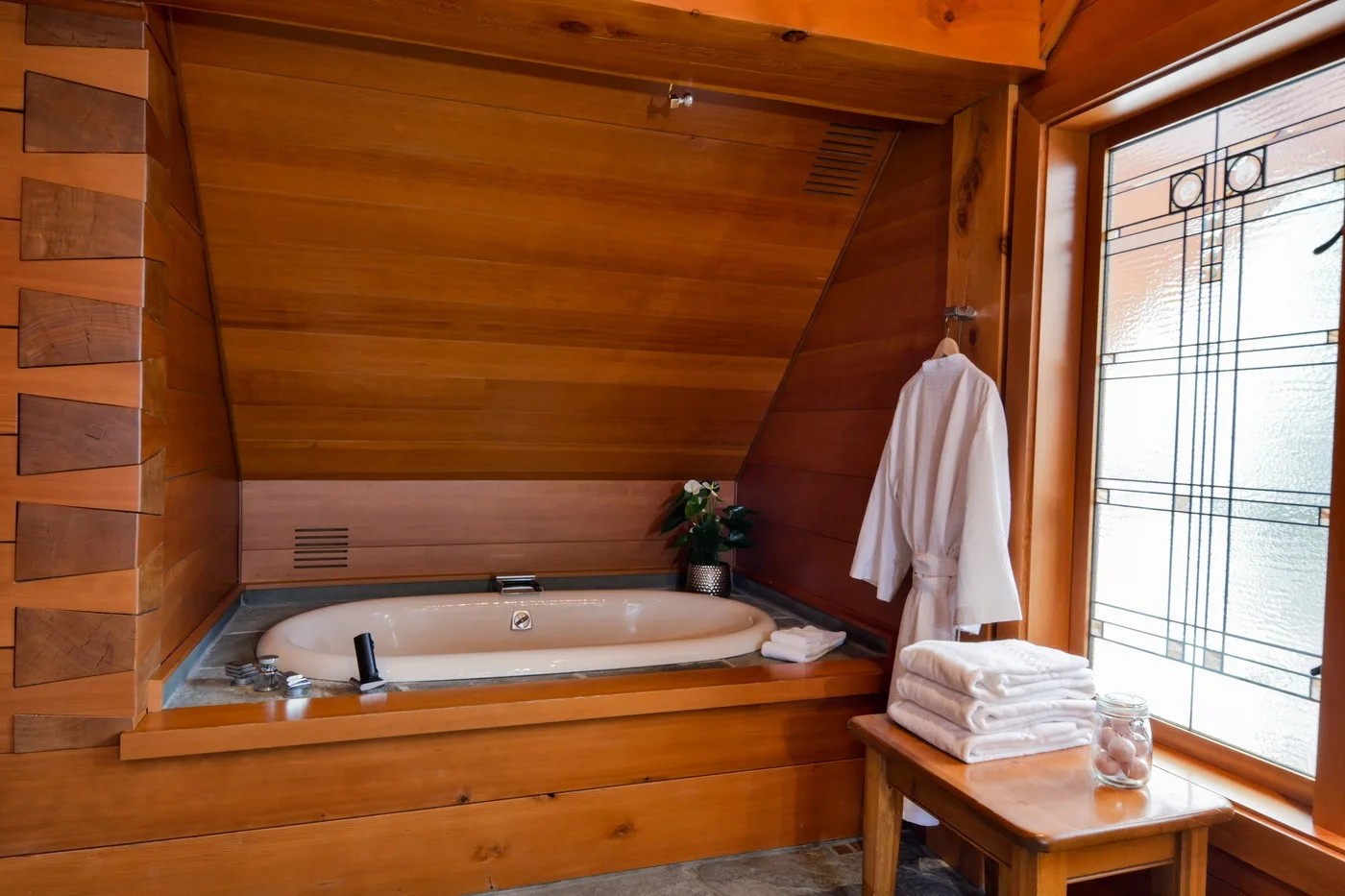 A wooden bathroom with a built-in bathtub and a bright window.