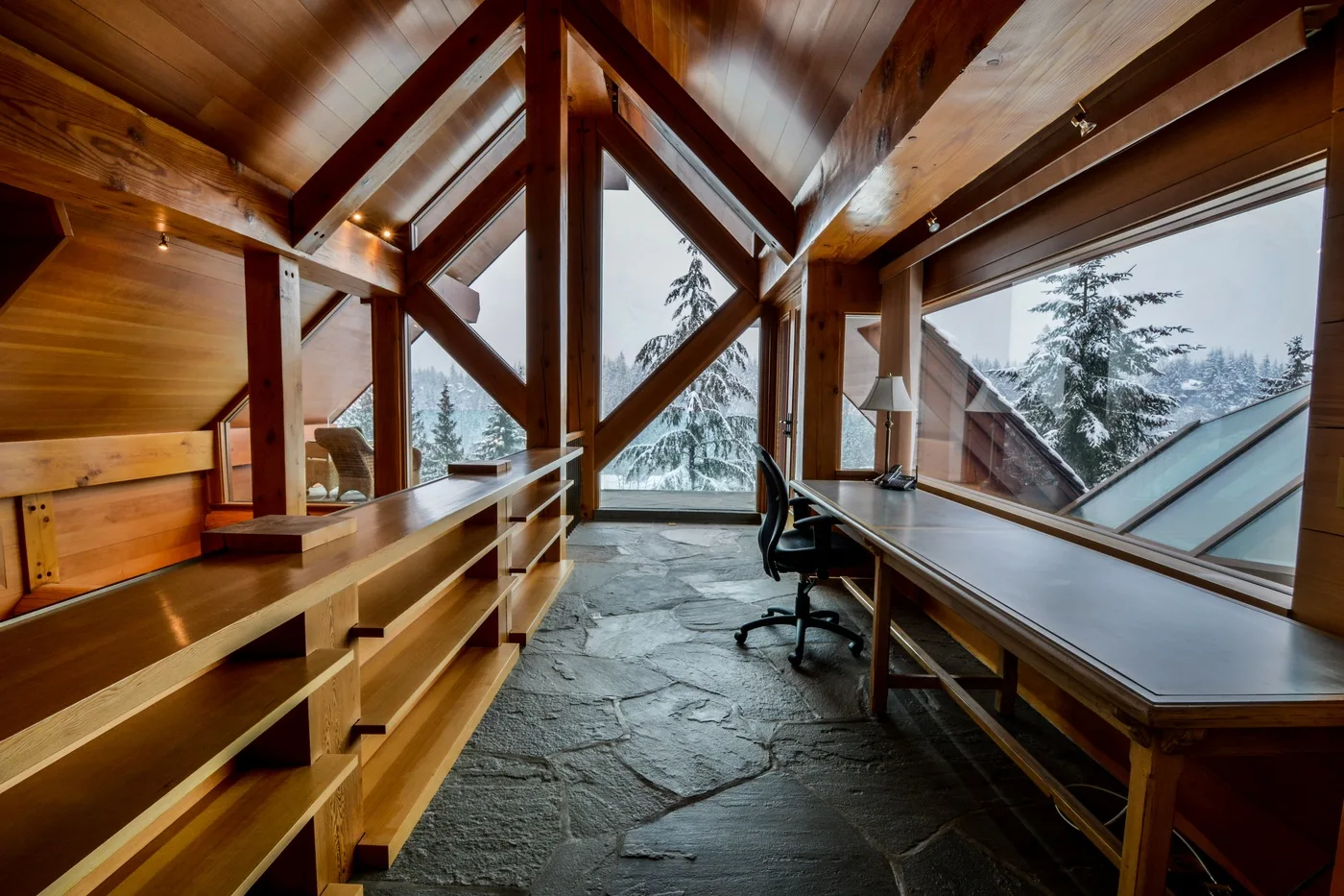 A wood-paneled workspace with long desks and large windows overlooking snowy trees.