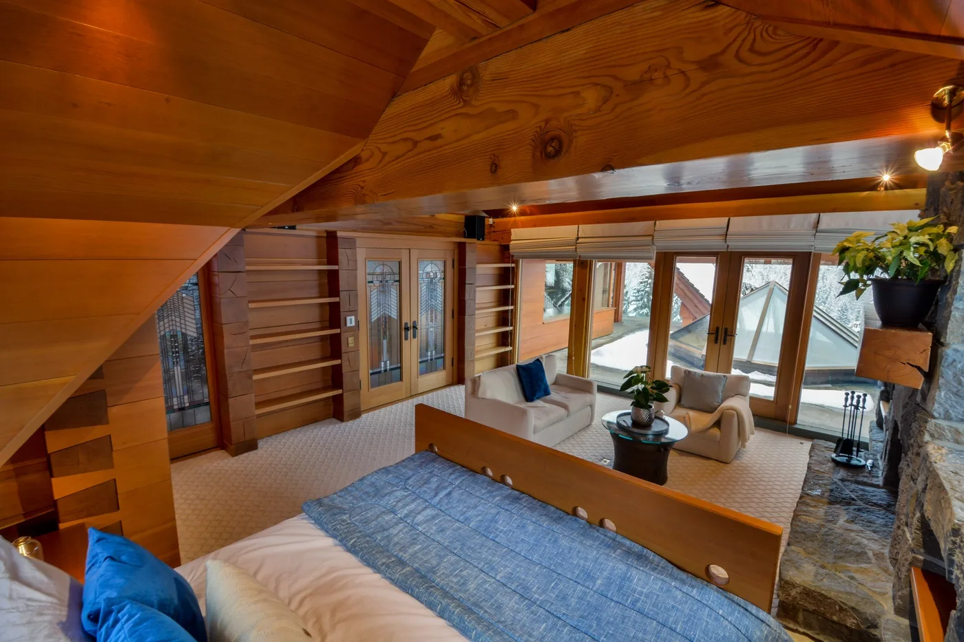 A wood-paneled living room has seating beside large windows and a stone fireplace.