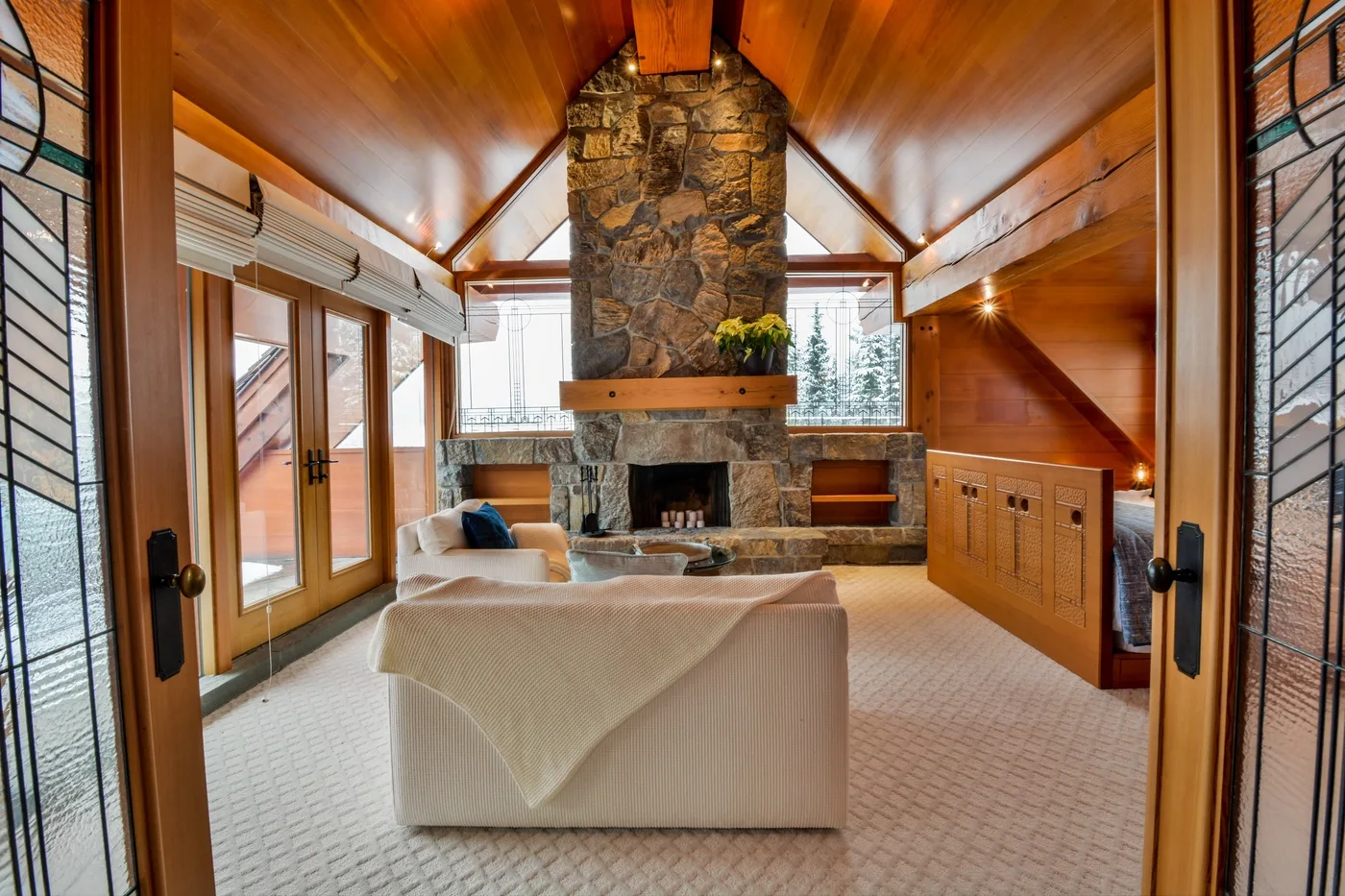 A living room with a stone fireplace and seating beneath a wood-paneled ceiling.