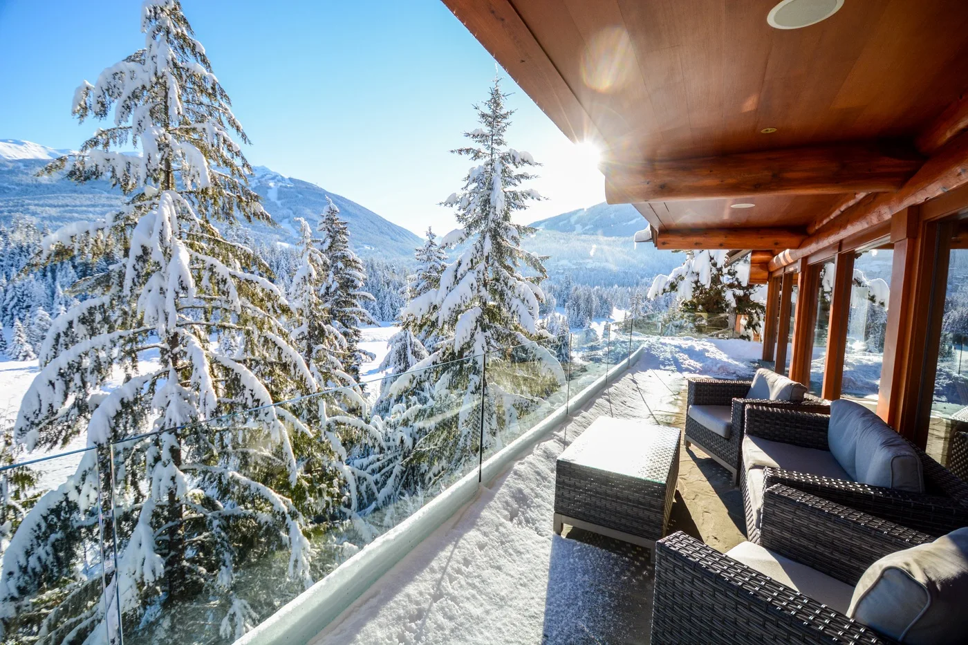 A snowy balcony with outdoor seating overlooks a mountain landscape.