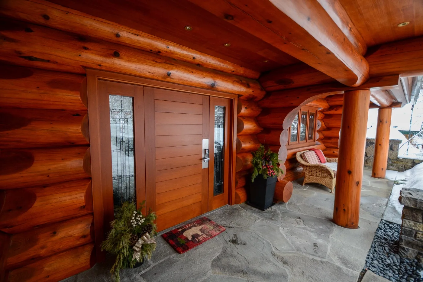 A covered log-cabin entrance with a wooden door and potted plants.