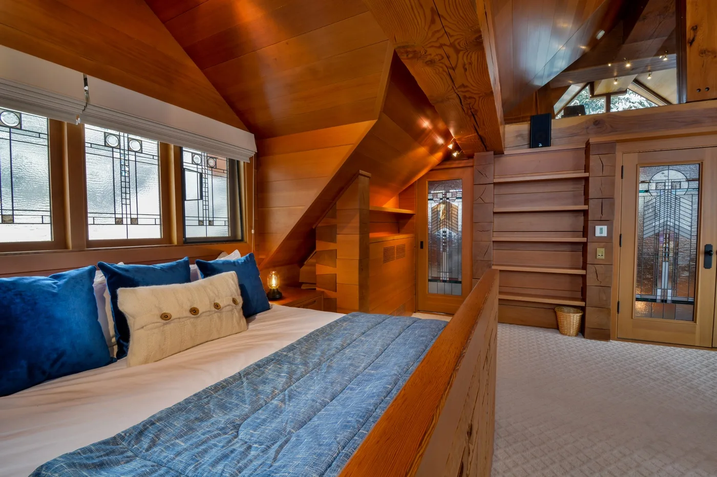 A bedroom with a bed beneath a sloping wooden ceiling and windows.