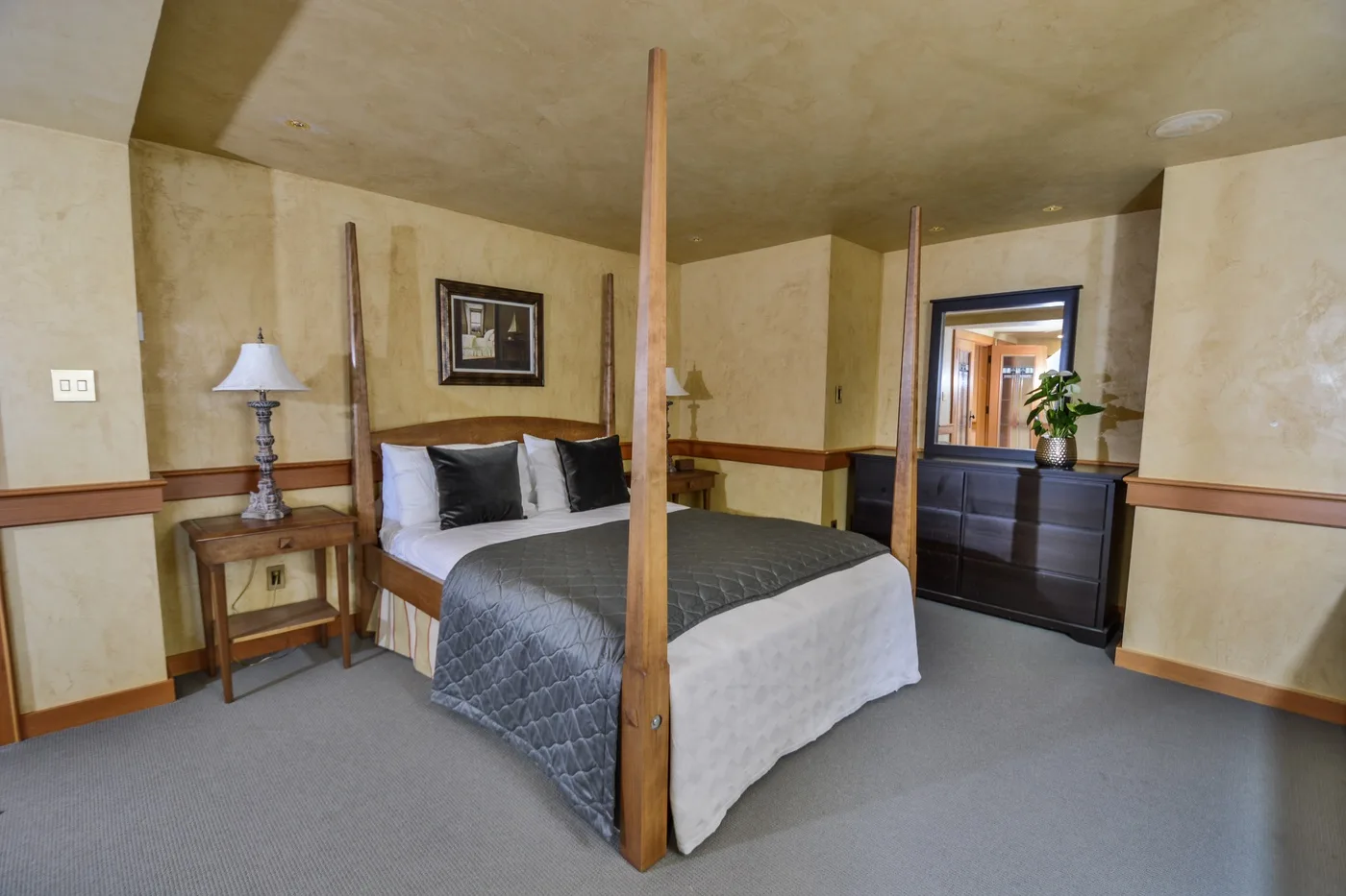 A bedroom with a four-poster bed, bedside table, and dresser.