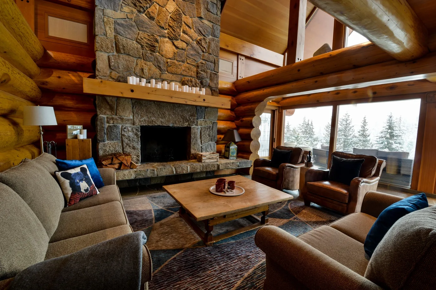 A rustic living room with seating arranged around a stone fireplace.