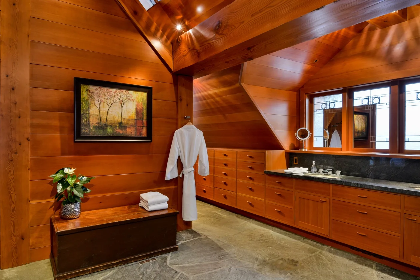 A wood-paneled bathroom with a long vanity, framed artwork, and a robe hanging on the wall.
