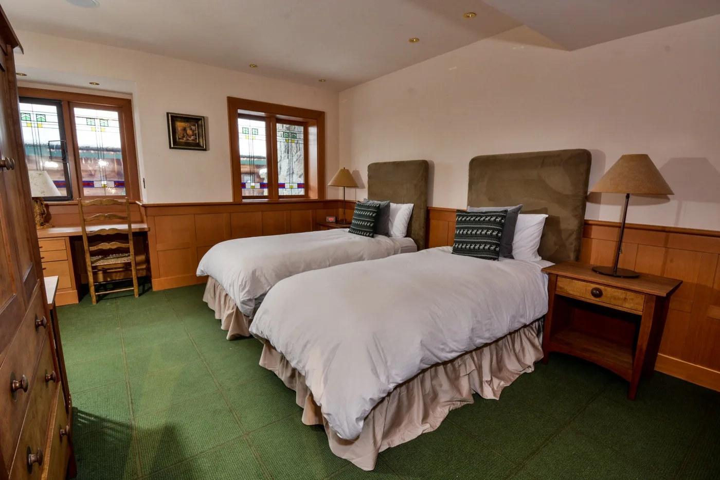 A bedroom with two beds, wood-paneled walls, and green carpeting.
