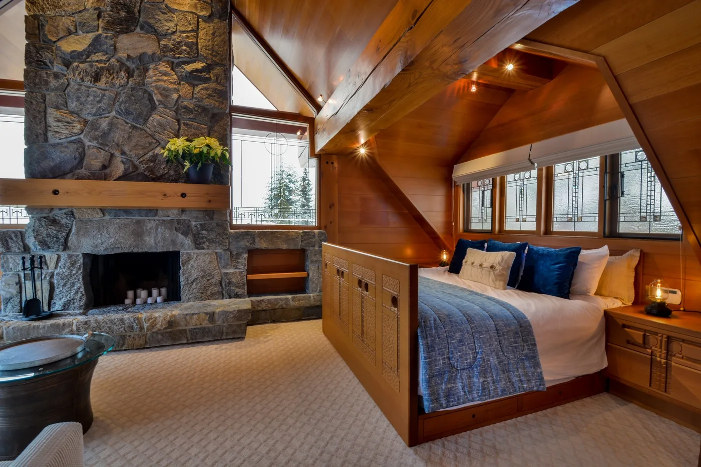 A wood-paneled bedroom with a bed beside a large stone fireplace.