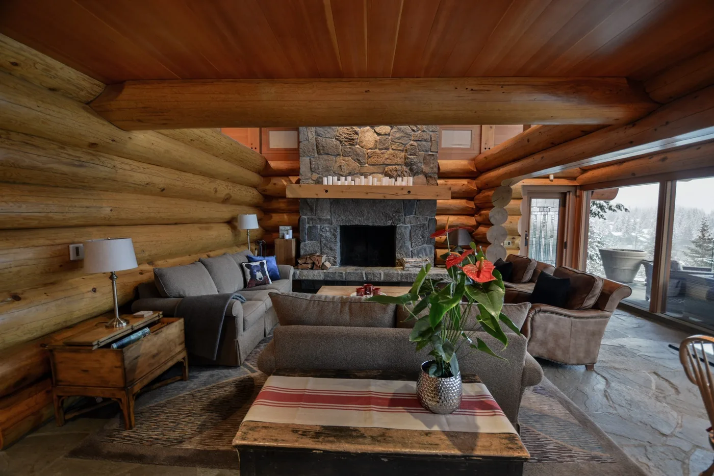 A rustic log-cabin living room with seating arranged around a stone fireplace.