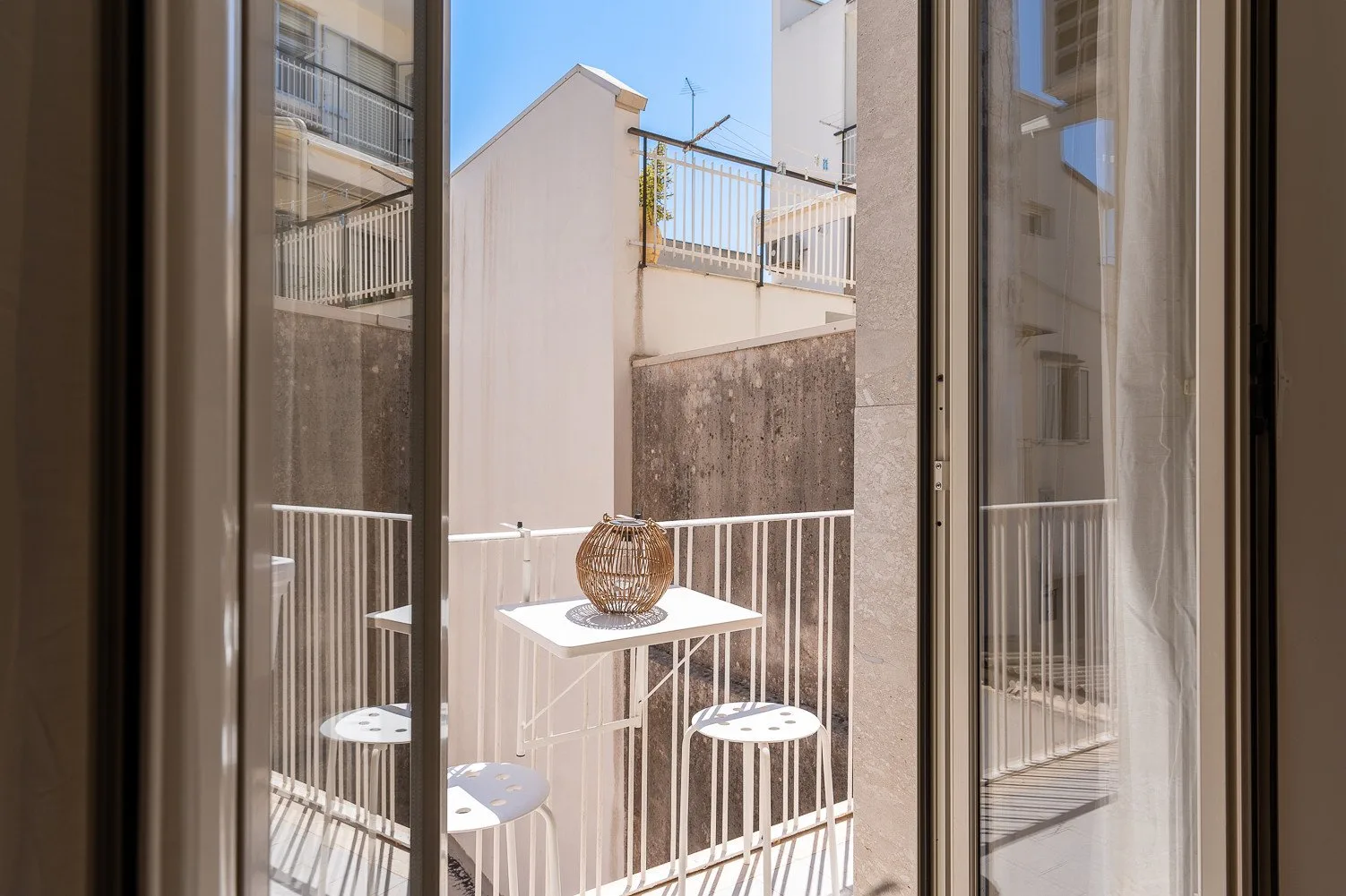 Se ve una pequeña zona de estar al aire libre con una mesa y taburetes a través de puertas de vidrio.