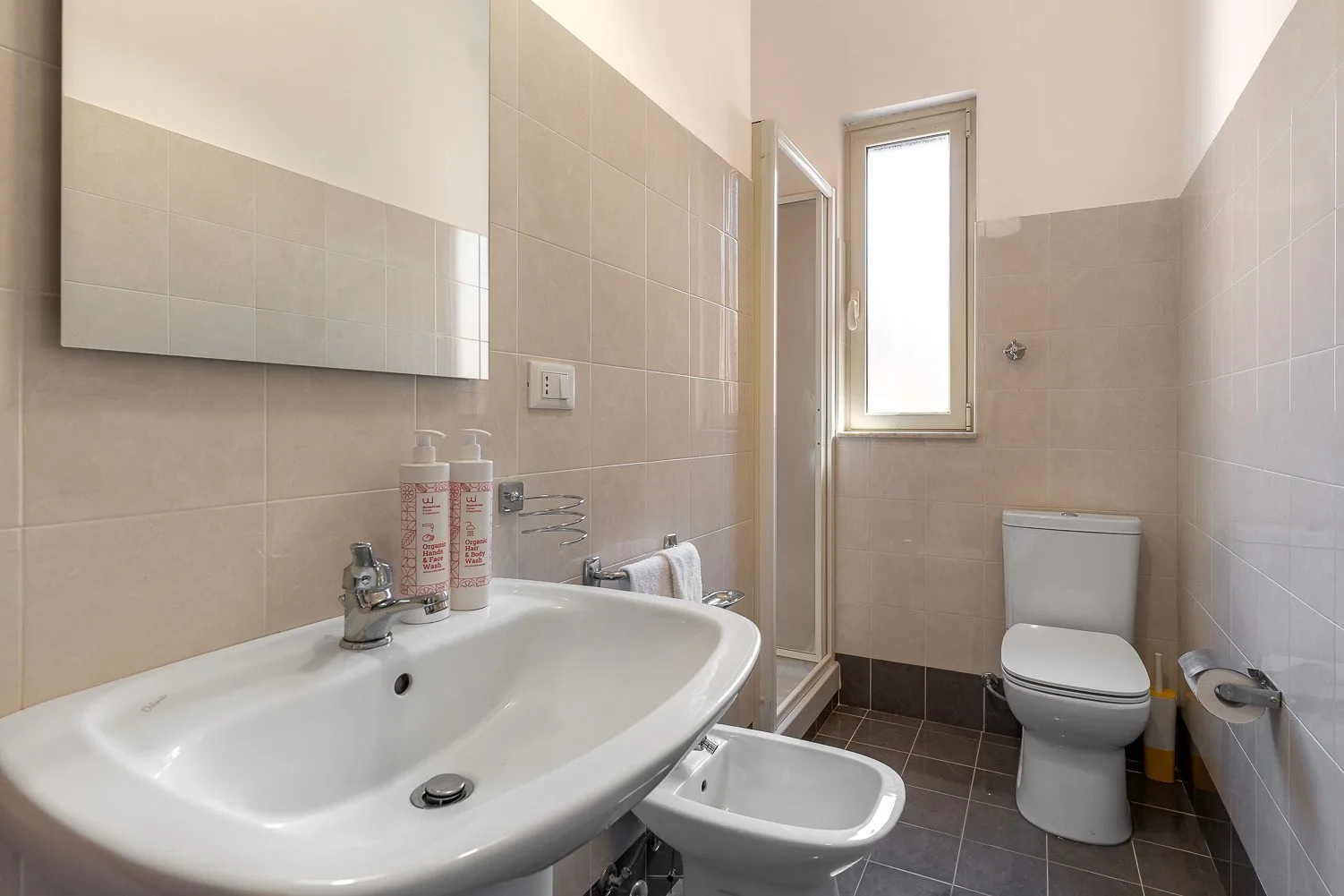 A tiled bathroom with a sink, toilet, and a window.