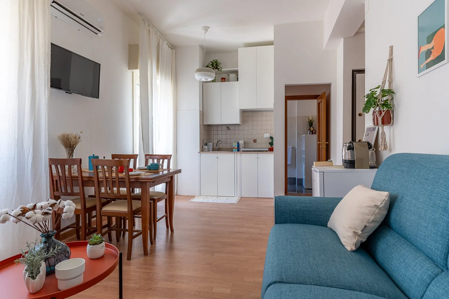 A bright living and dining area with a compact kitchen and blue seating.