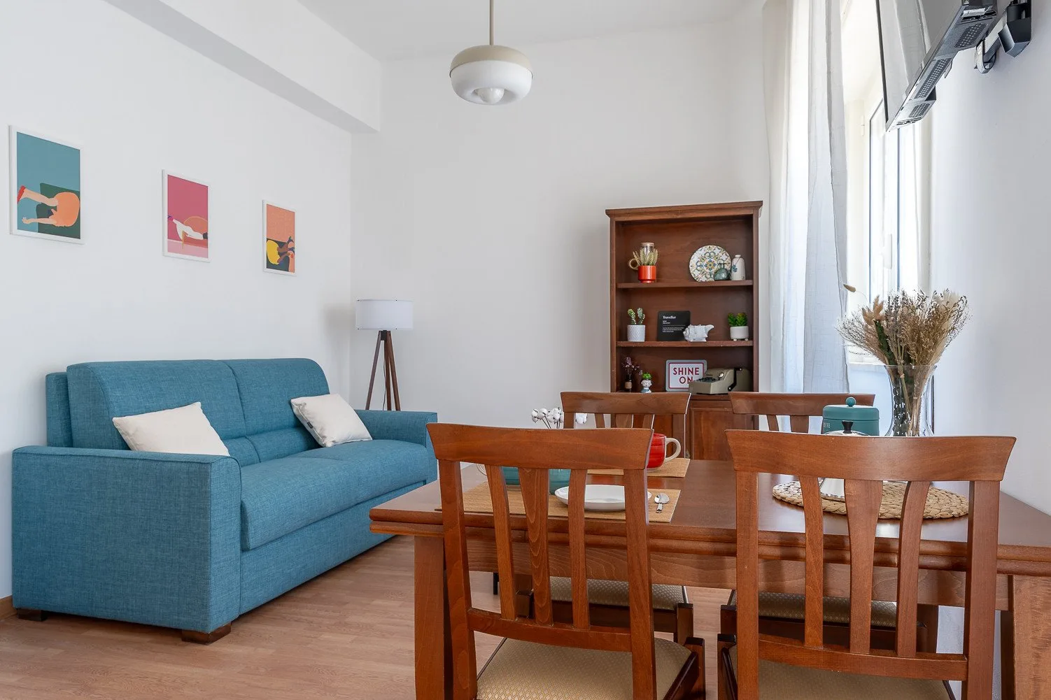 Una zona de comedor y sala de estar con mesa de madera y asientos azules junto a grandes ventanas.