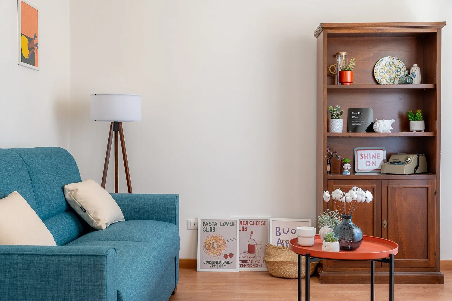 A living room with teal seating beside a wooden bookcase and round table.