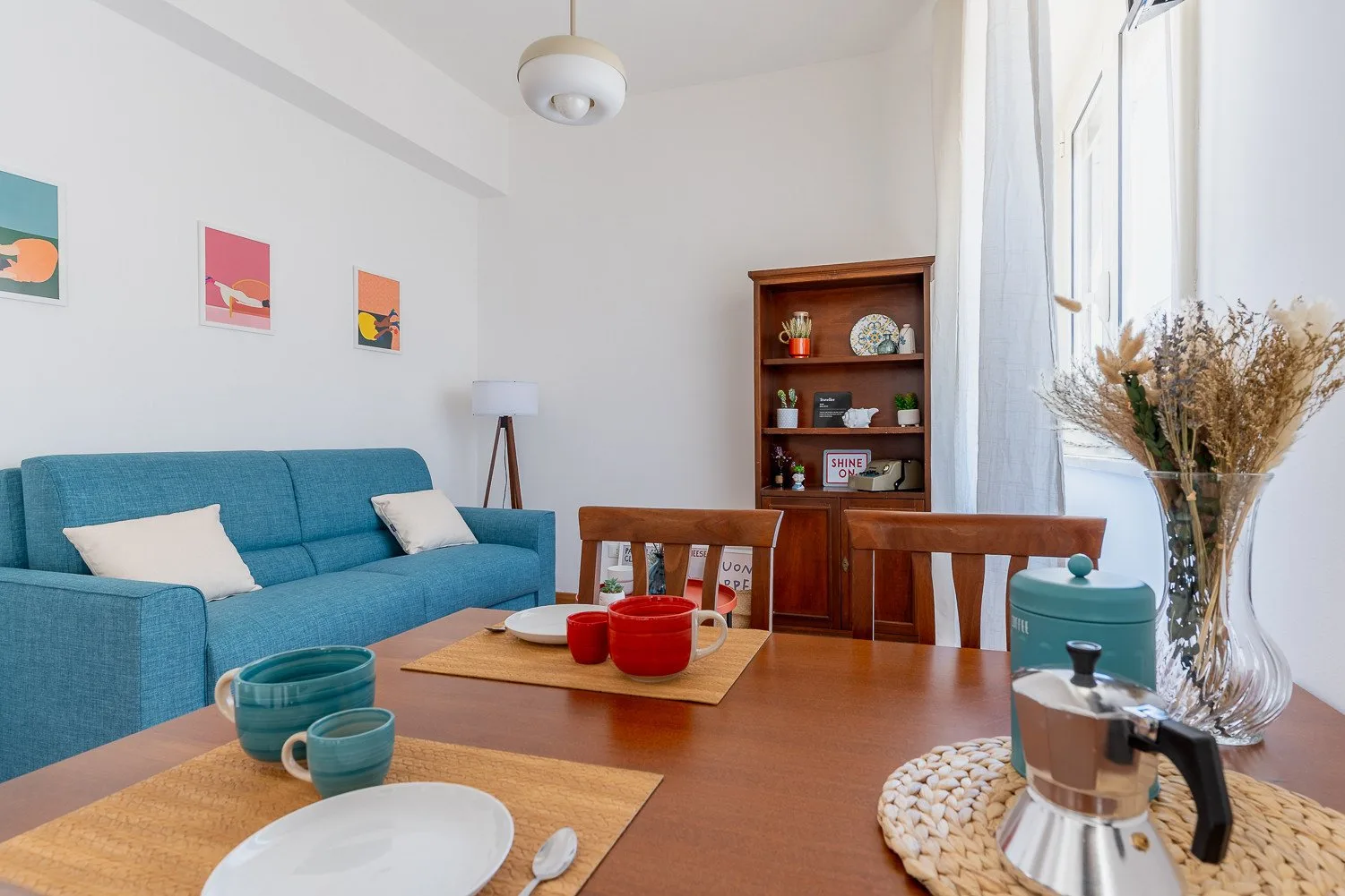 A bright living room with a blue sofa, wooden table, and open shelving.