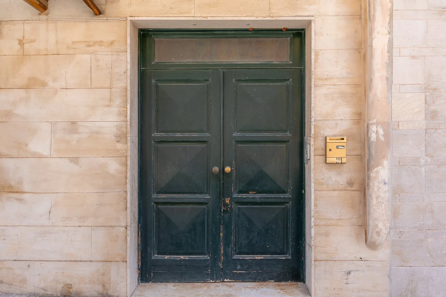 A dark green double door set into a pale stone wall.
