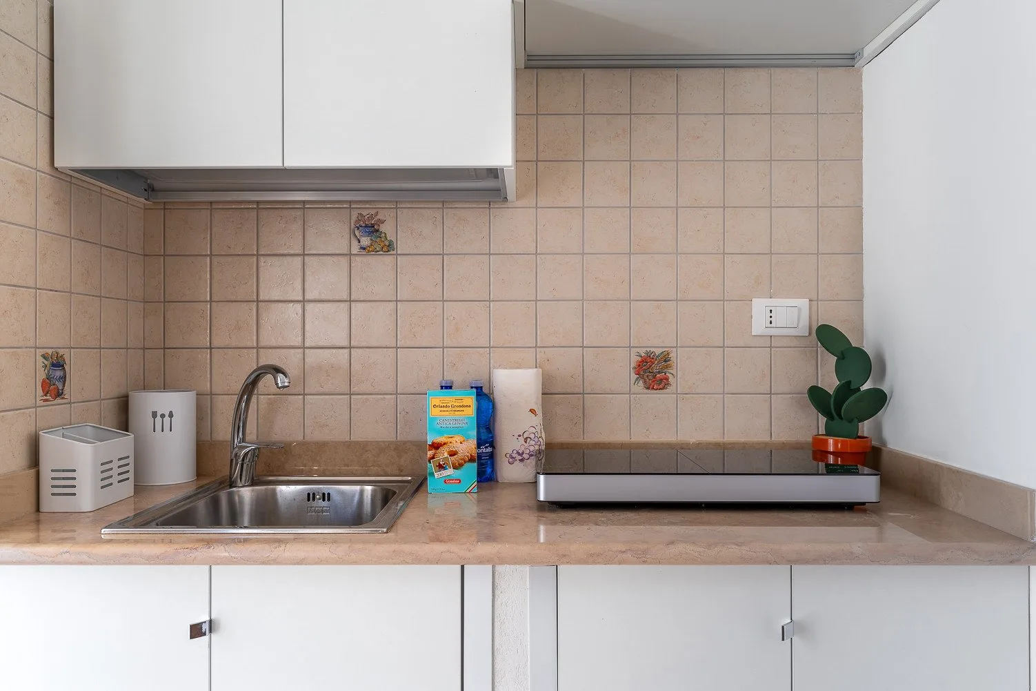 A tiled kitchen counter with a sink, faucet, and upper cabinets.