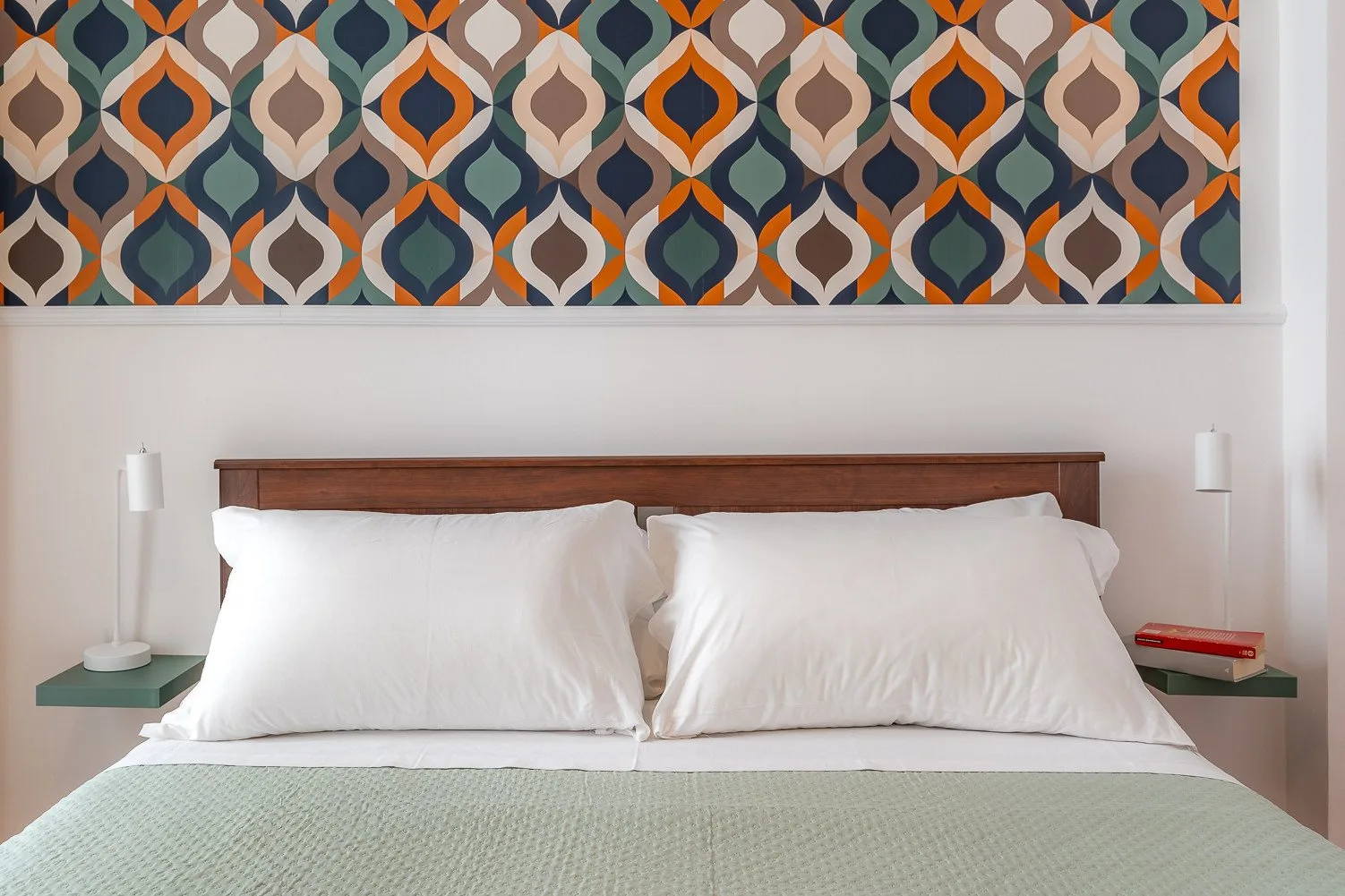 Un dormitorio con una cama bajo un mural geométrico colorido.