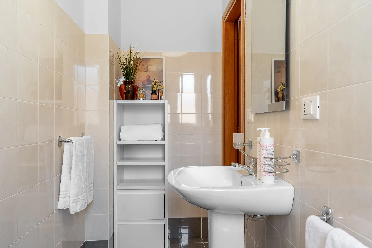 A tiled bathroom with a sink, mirror, and shelving.