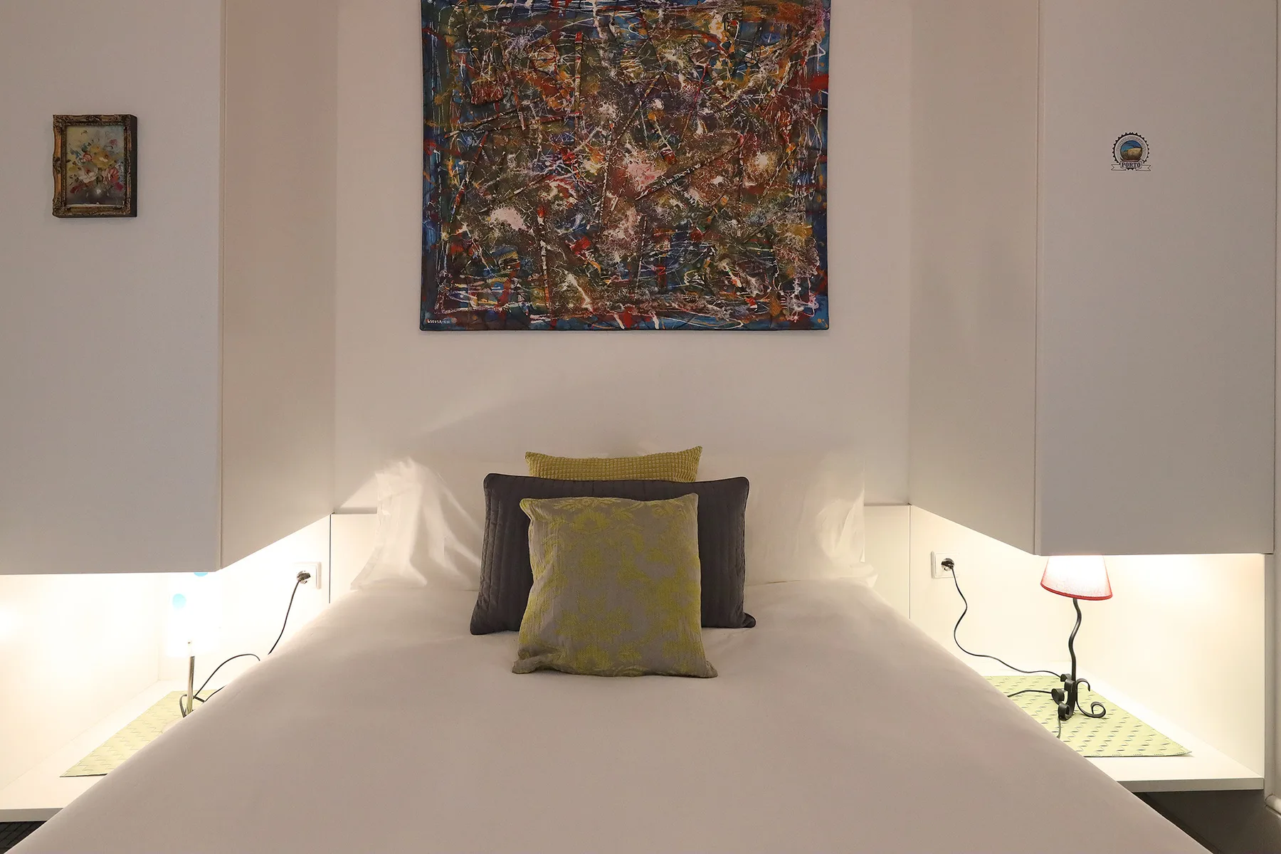 A bedroom with a bed, decorative pillows, and colorful artwork above the headboard.