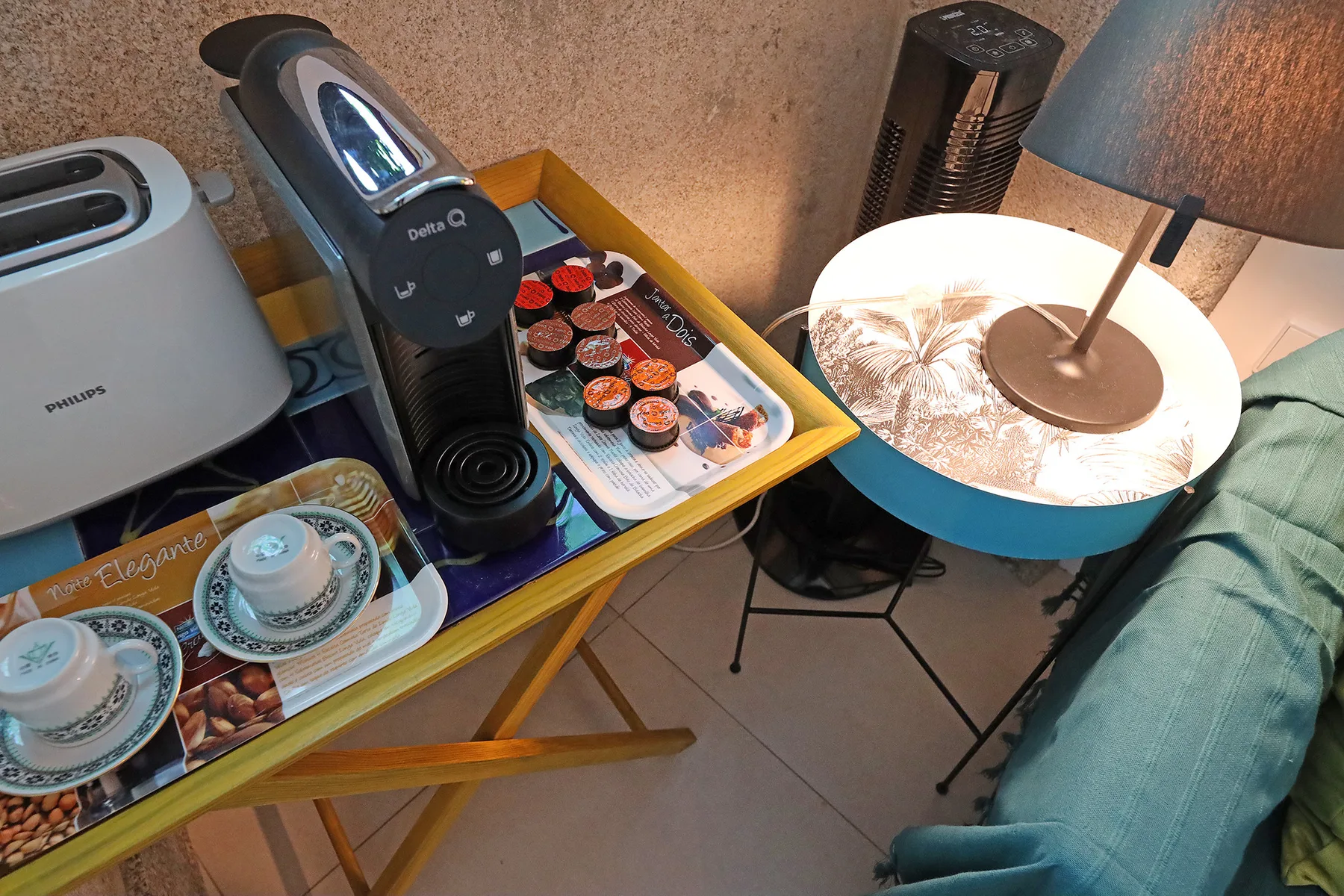A seating area with a small table, coffee machine, and cups.