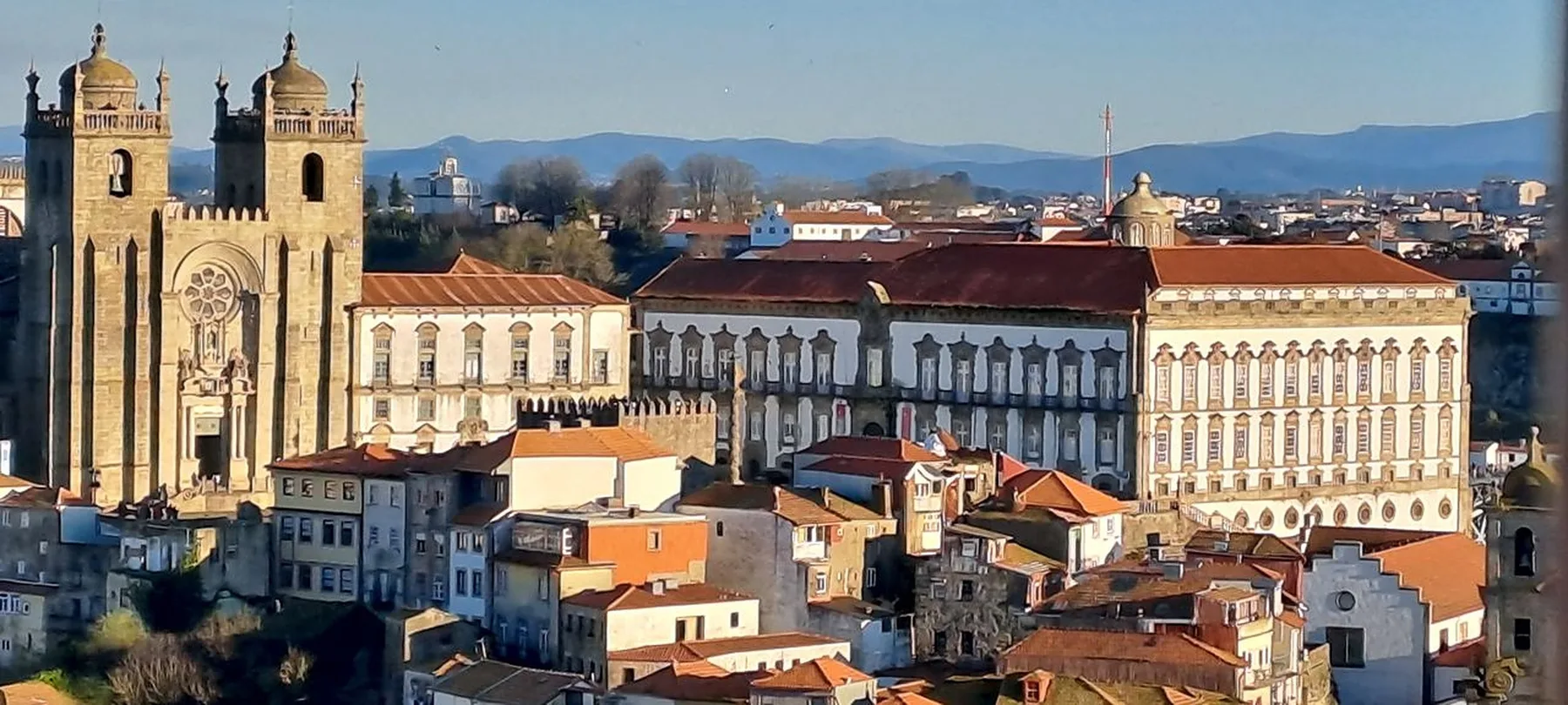 A cityscape of historic buildings and church towers beneath distant hills.