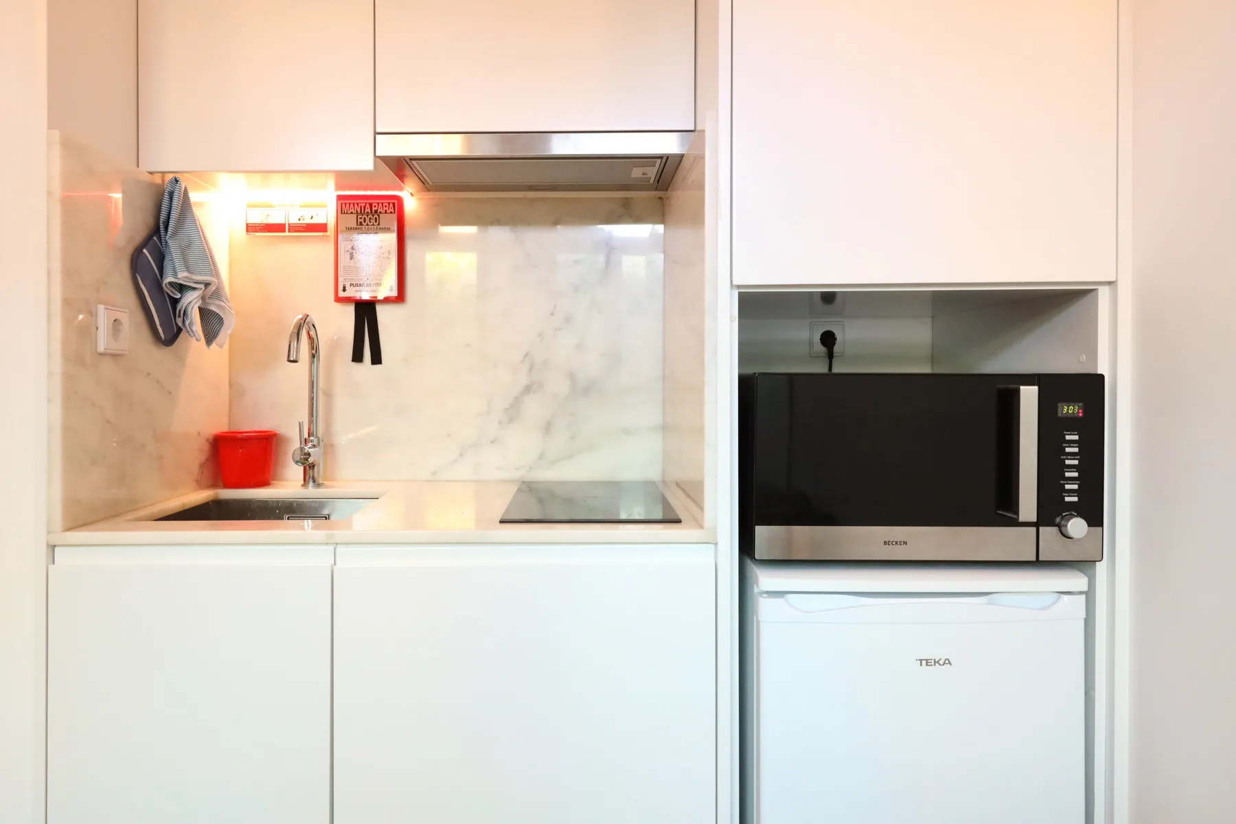 A compact kitchen with a sink, cooktop, microwave, and refrigerator.