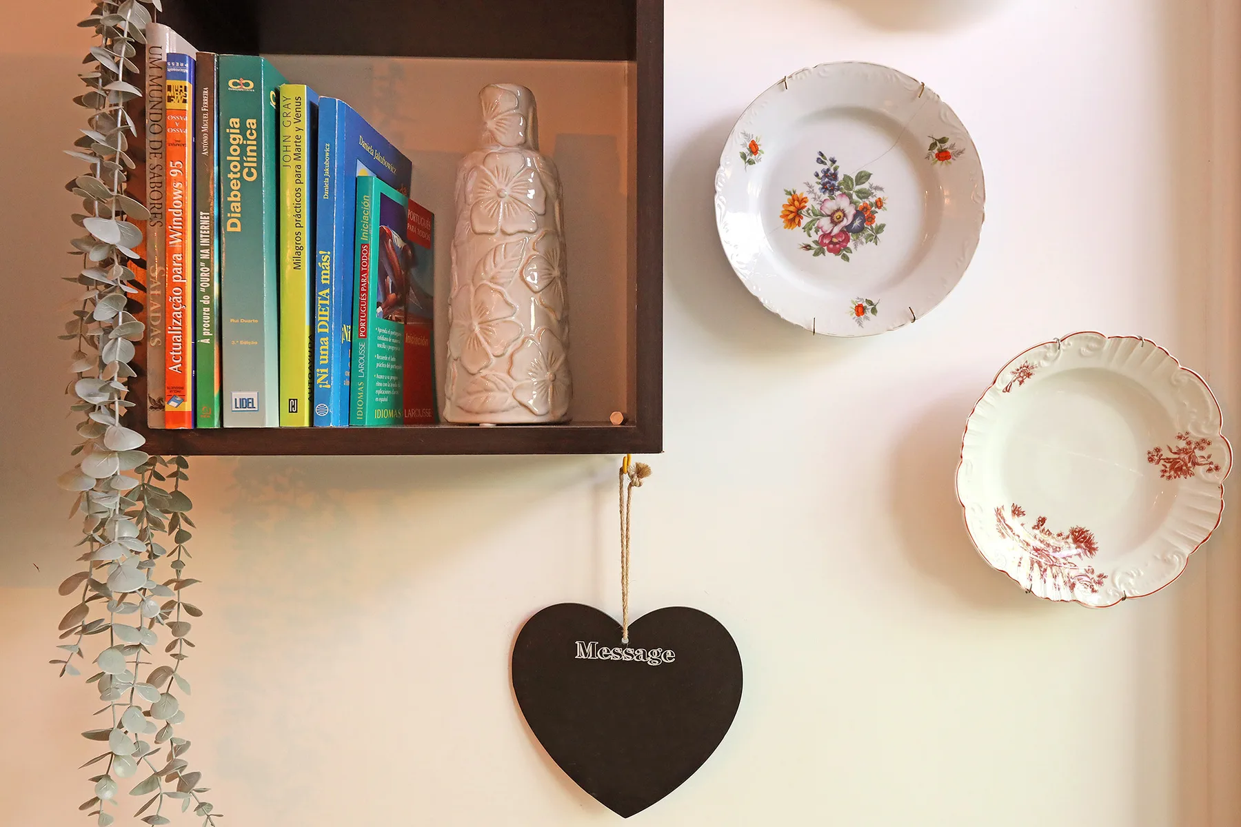 A decorative wall display features a bookshelf, hanging heart, and floral plates.