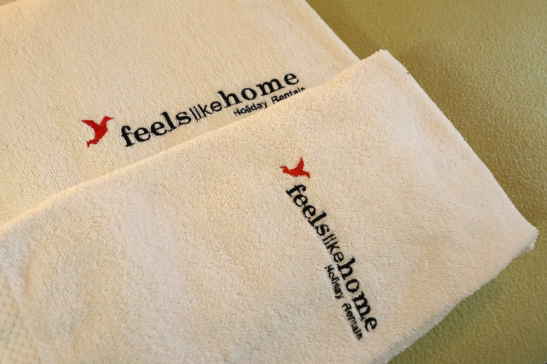 Two folded white towels display a small red bird and black lettering.