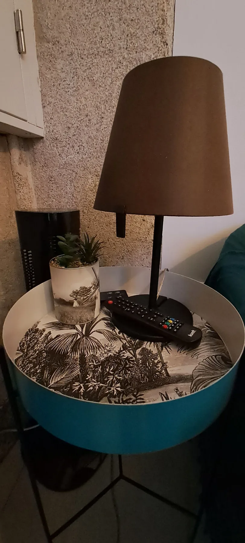 A small round side table holds a lamp, a plant, and a remote.