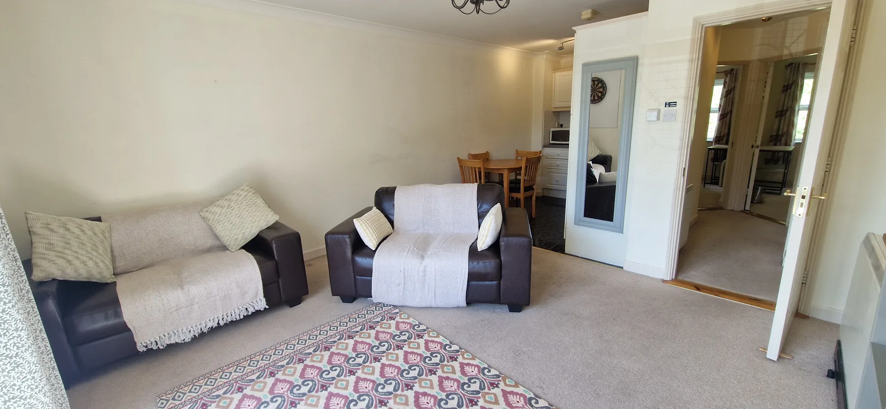 A living room with two seats, a patterned rug, and a dining table in the background.