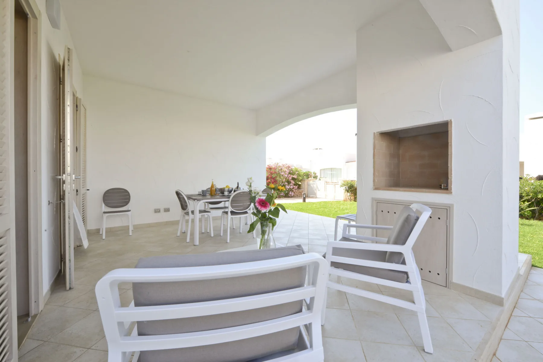 A covered patio with seating and a dining table opens onto a garden.