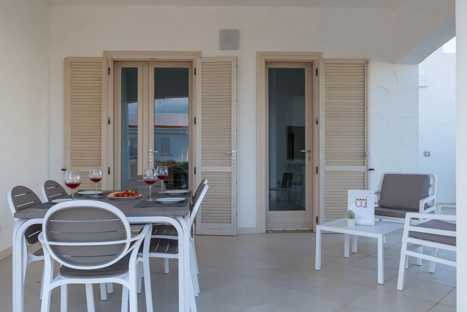 A covered patio has a dining table and seating beside glass doors.