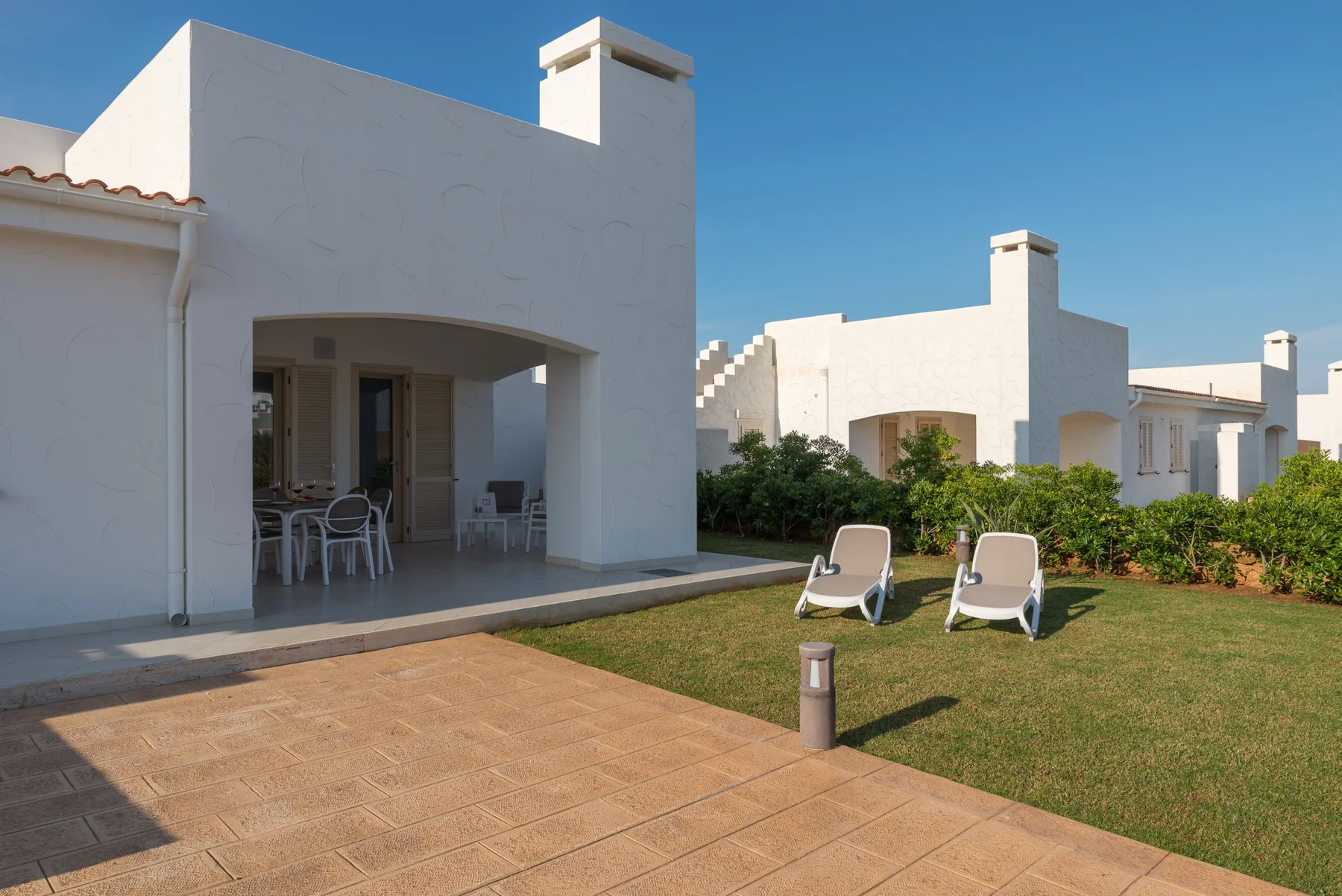 A white patio opens onto a tiled terrace and grassy garden.