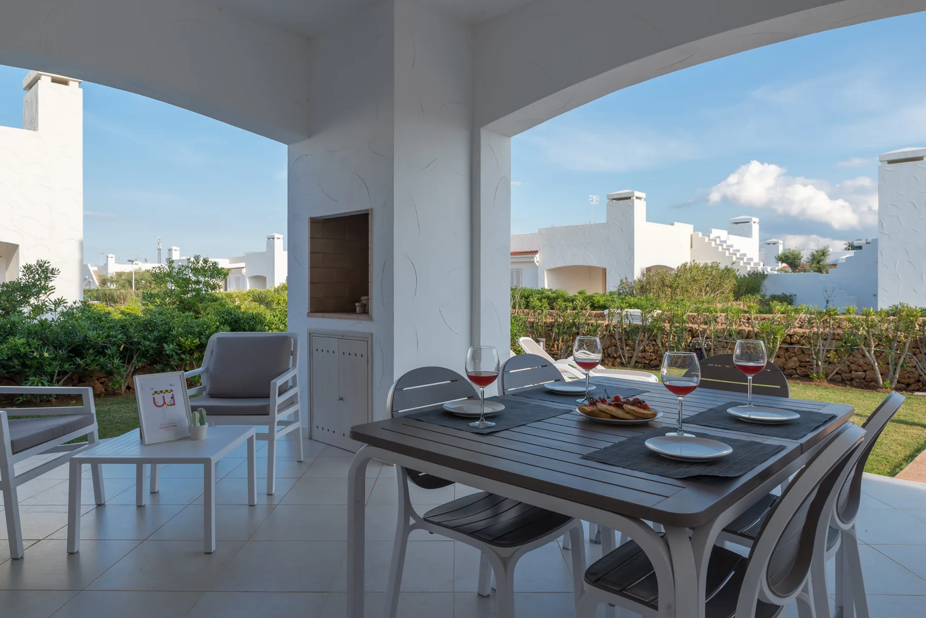 A covered patio dining area with a table and seating overlooking a garden.