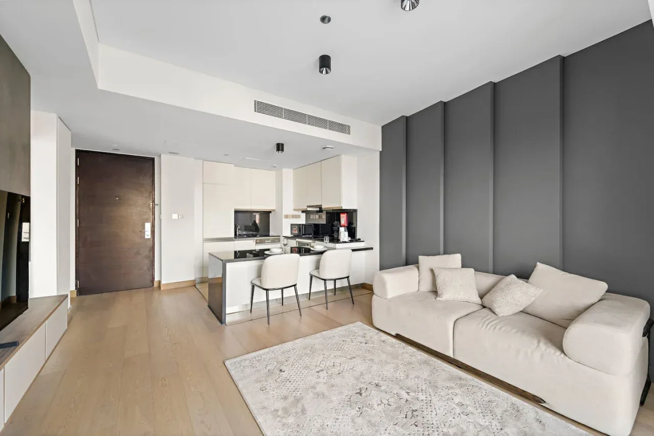 A modern living room with light seating beside an open kitchen and dining area.