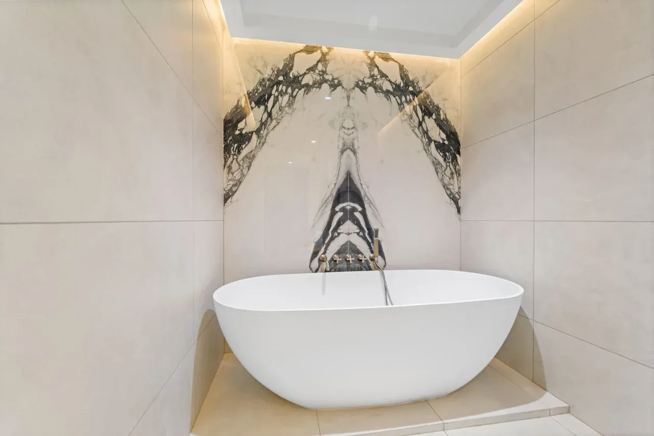 A freestanding bathtub sits against a marble-patterned bathroom wall.