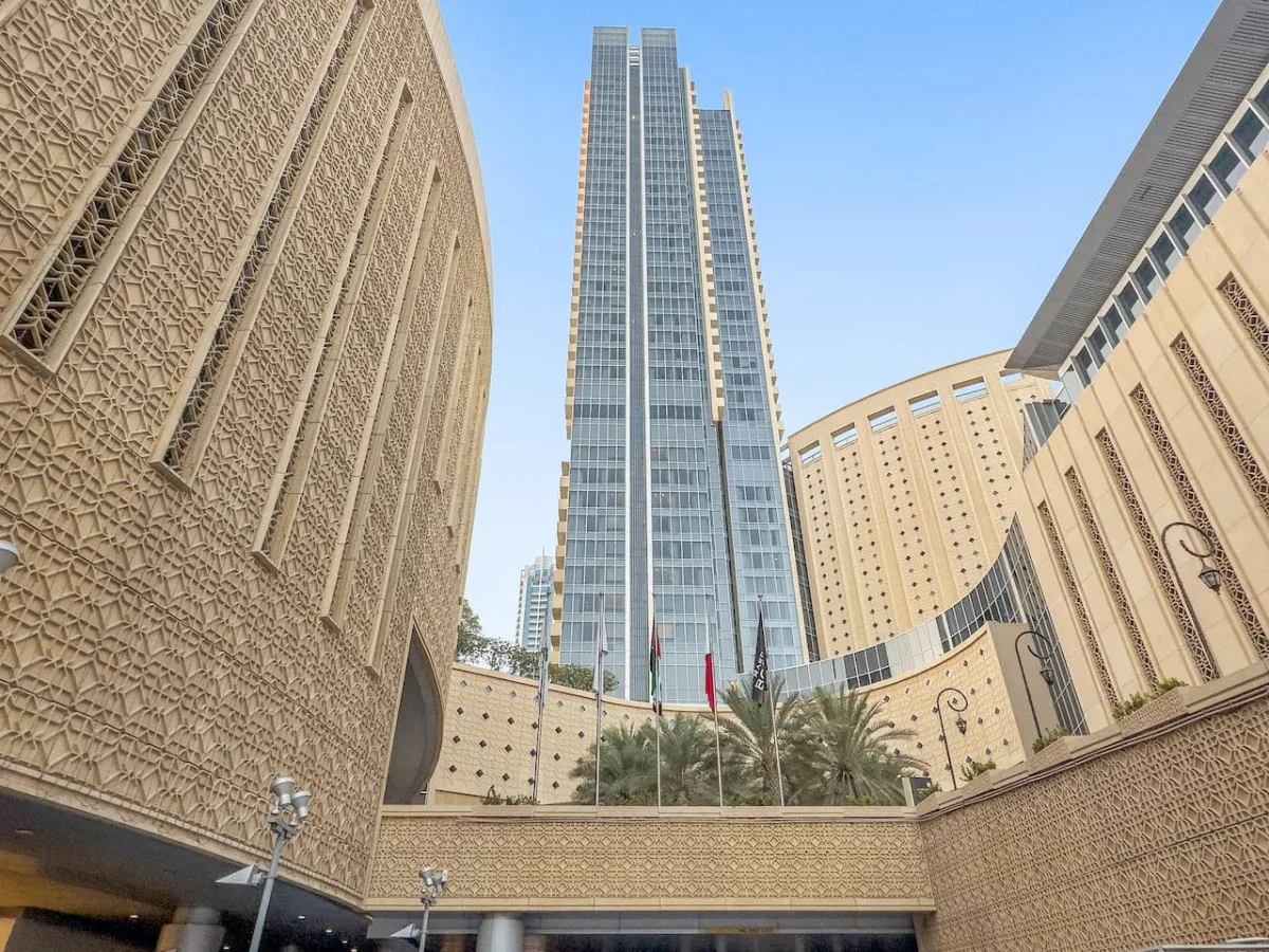 A tall glass tower rises above an ornate courtyard with palm trees.