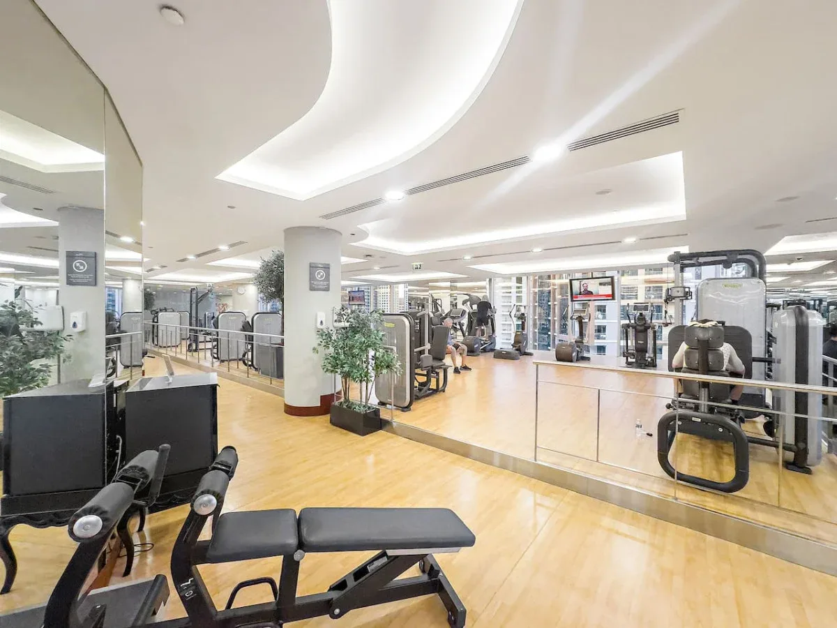 A bright gym with exercise machines, weight equipment, and a wood-toned floor.