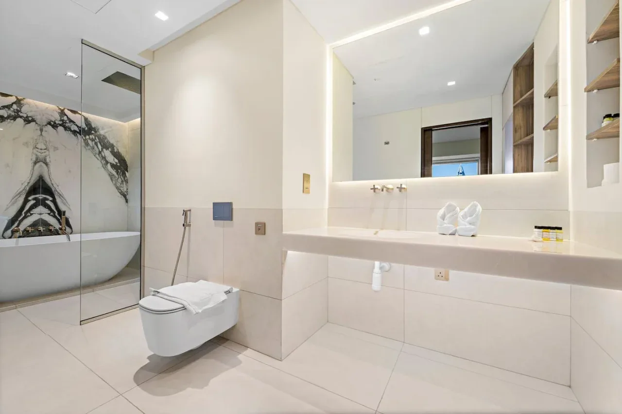 A bright bathroom with a bathtub, wall-mounted toilet, and broad vanity.