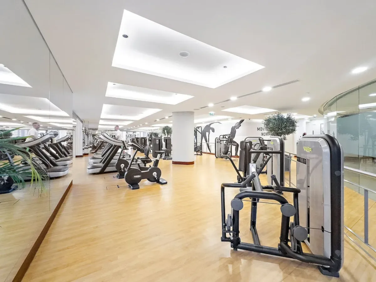 A bright gym with rows of exercise machines and a light wood floor.
