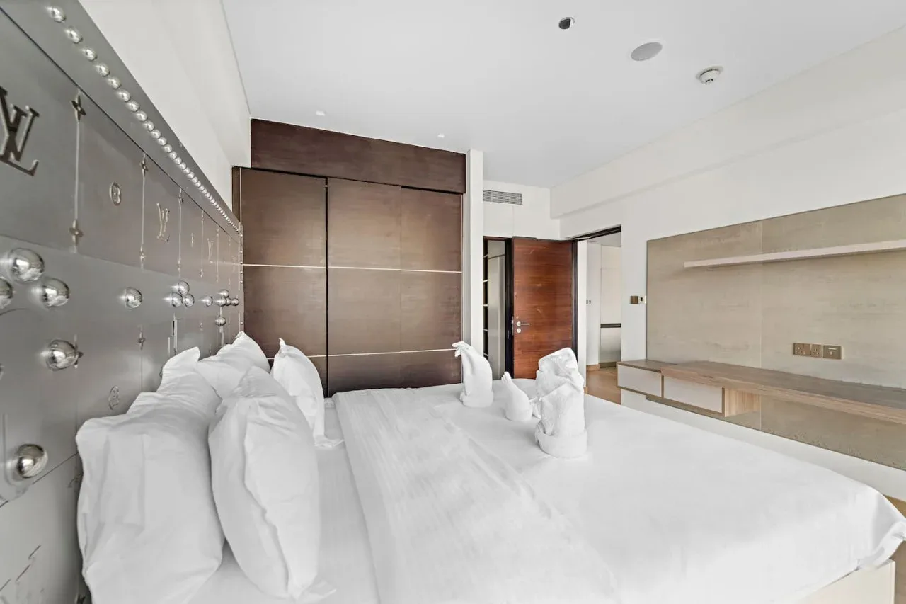 A bright bedroom with a large bed, white bedding, and built-in wall storage.